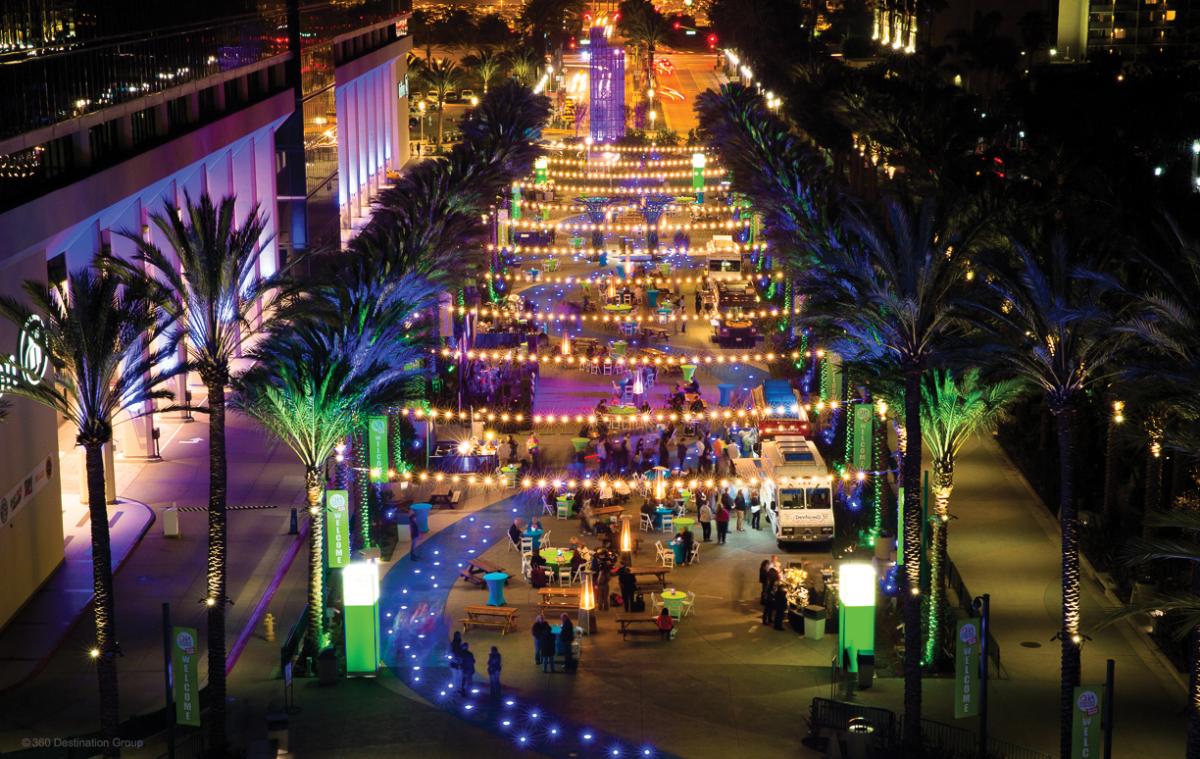 An aerial view of Grand Plaza, Anaheim. Multicolored lights make palm trees and buildings blue, purple and orange.