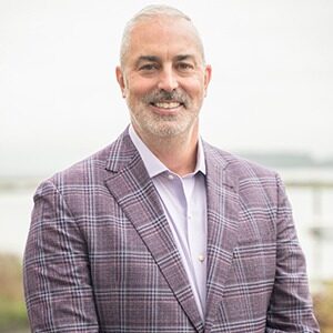 A portrait of Jon McGaunn. He is an older white man with a gray plaid suit jacket.