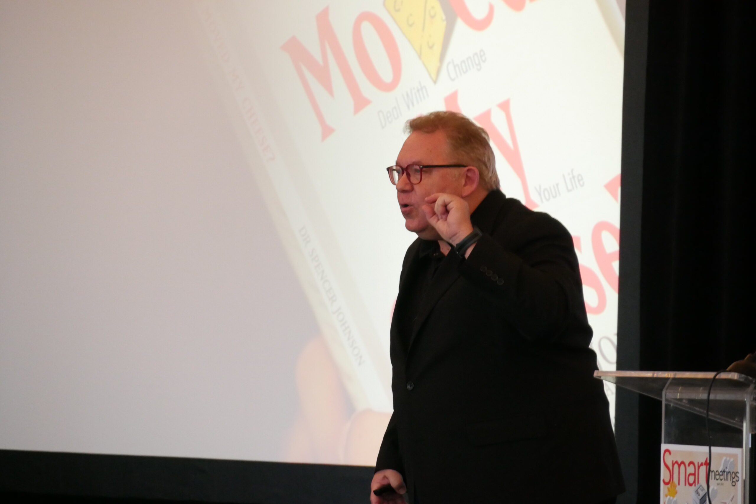 A picture of Keith Harmeyer speaking onstage in front of a projector.