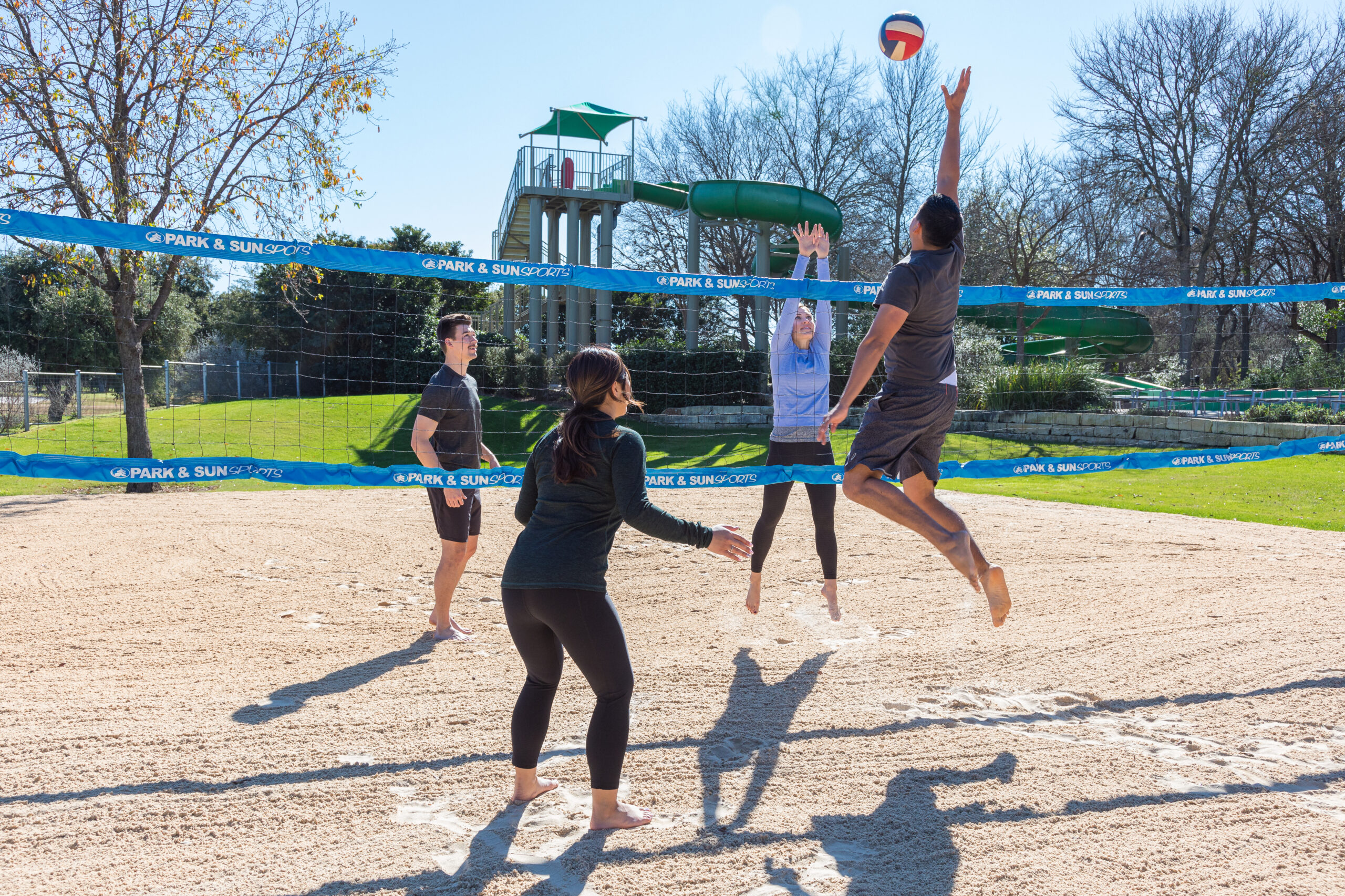Four adults playing beach volleyball in a public park.