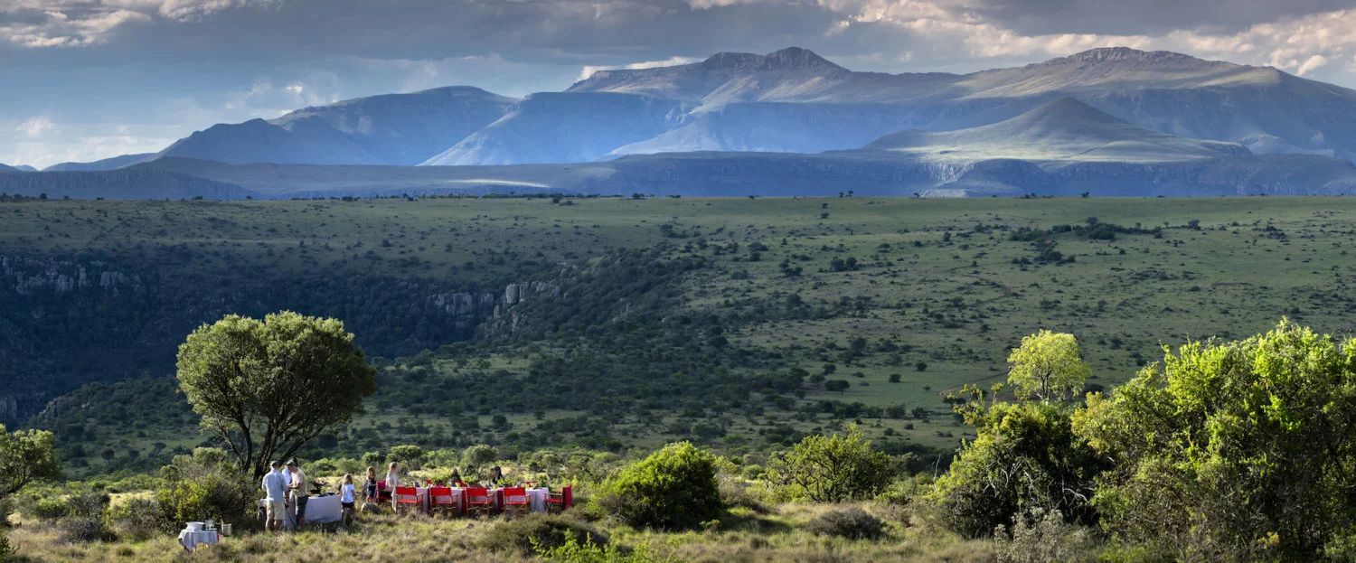 A small group of tourists eating at a red table on a plain with a mountain in the background