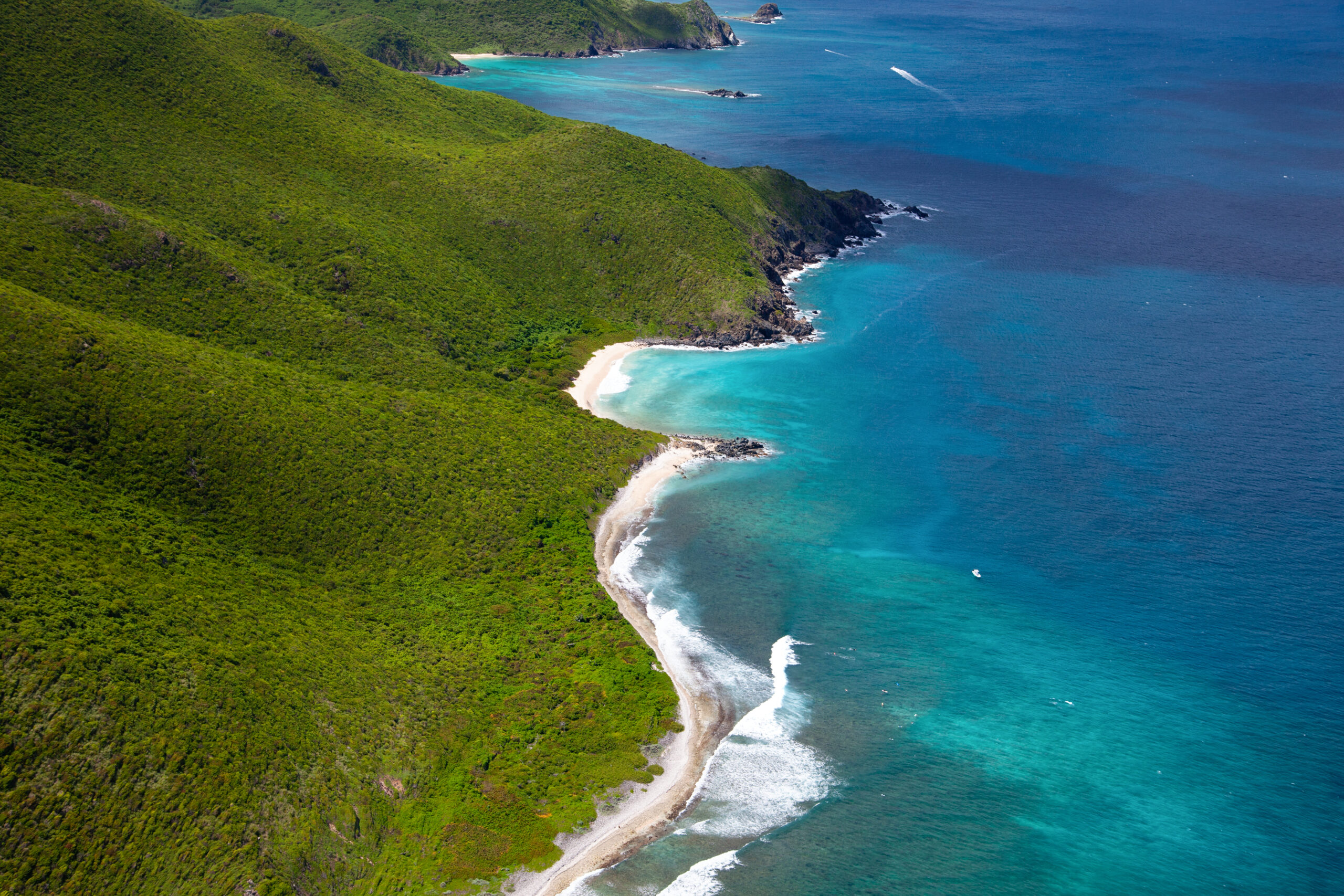 A aerial shot of the beach of Sint Maarten. Forested hills slope down to the ocean.
