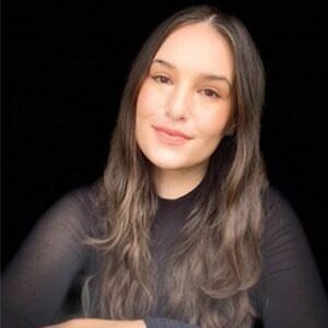 A portrait of Brennan Rosonet. She is a young white woman with long brown hair and a sheer black blouse.