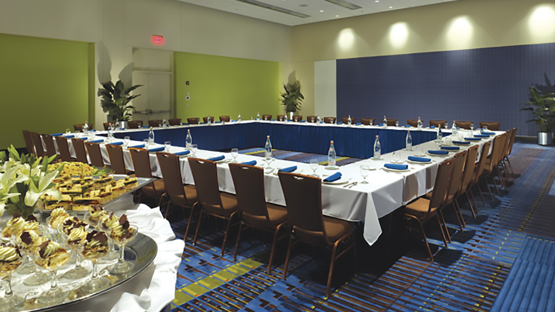 The boardroom at Ocean Center. The walls and carpet are green and blue. Chairs are arranged around a large square table. A dessert table is in front of the table.