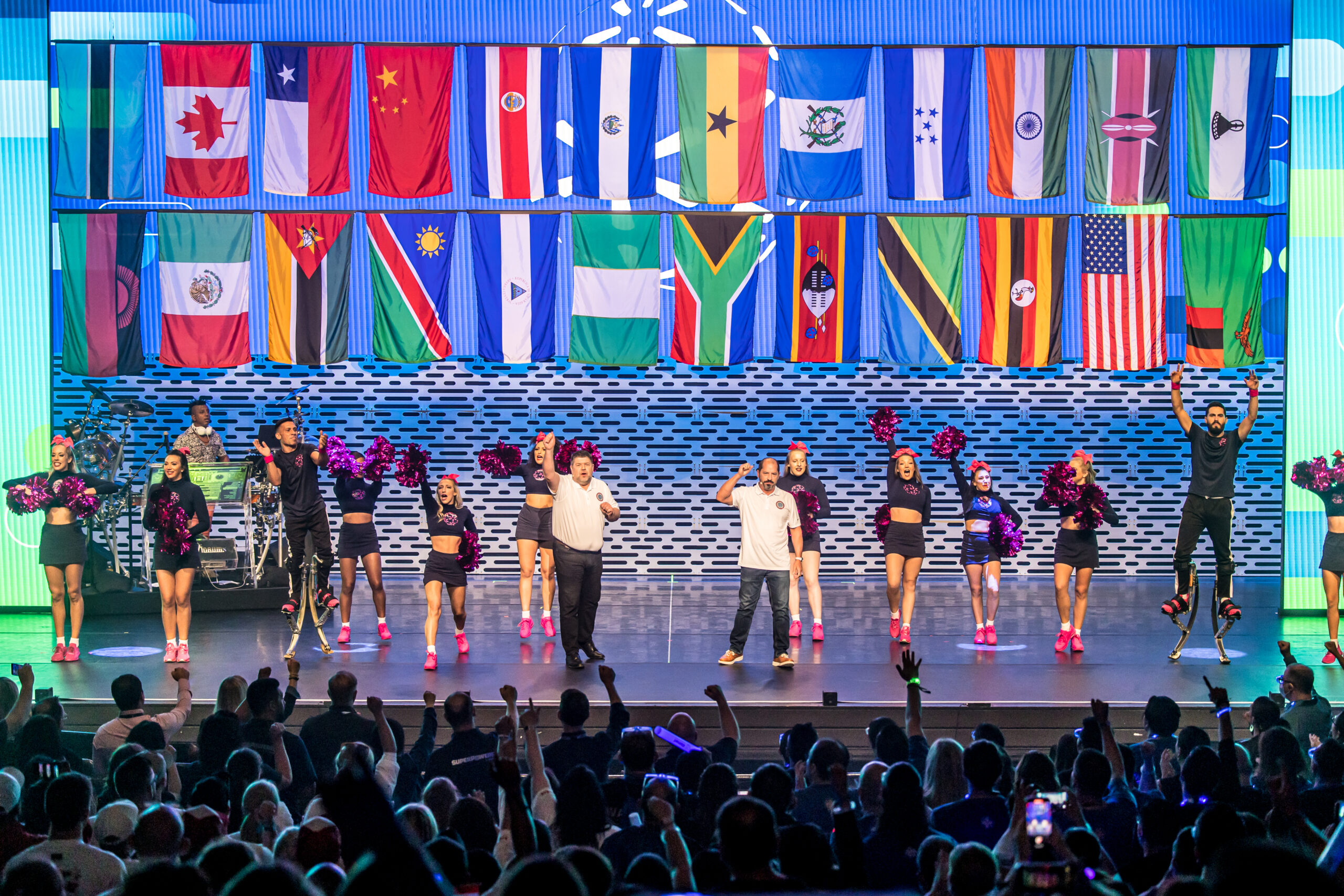 Speakers and cheerleaders stand onstage under a series of country flags for International Associates Celebration.