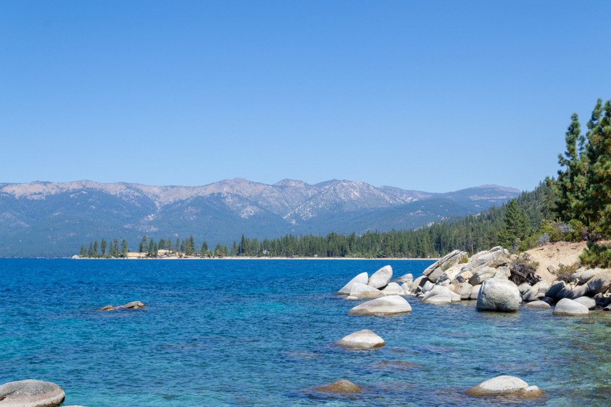 Lake Tahoe from the shoreline. The Sierra Nevada mountains are in the distance behind evergreen trees.