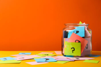 A stock image of a jar holding papers with question marks on them.