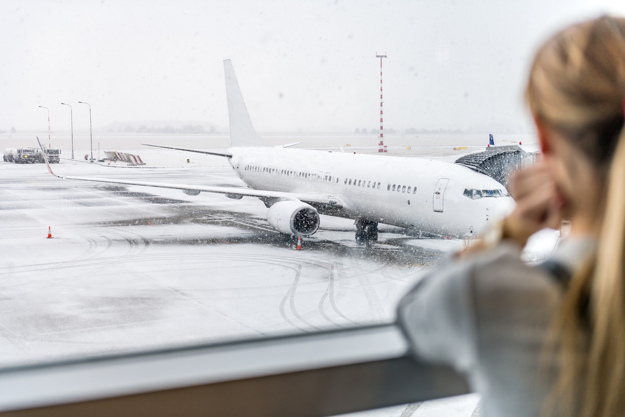 A woman in the foreground looks out of the window at an airplane parked at a gate.