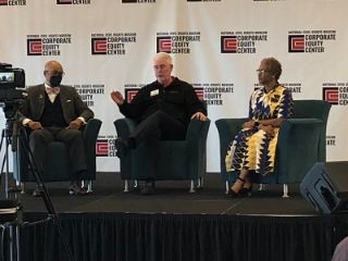 Three executives sitting in chairs on a stage.