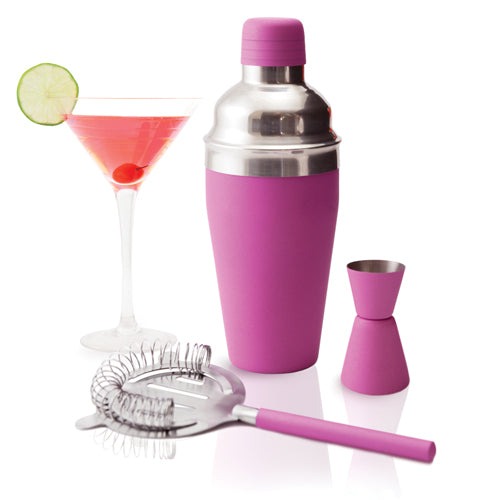 A pink camping cocktail set that includes a shaker, a shotglass, and a jiggler. A pink cocktail in a martini glass is next to the set.