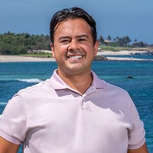 A portrait of Denis Espina. He is a Mexican man with combed black hair and a lavender collared shirt.