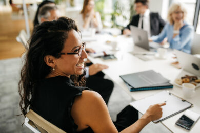 over-the-shoulder angle of one meeting with five colleagues and laughing in a conference room