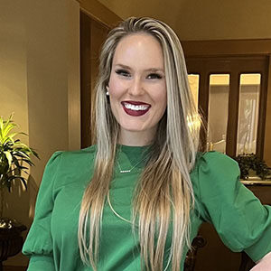 A portrait of Isabella Marciante. She is a blonde woman with a green blouse and red lipstick