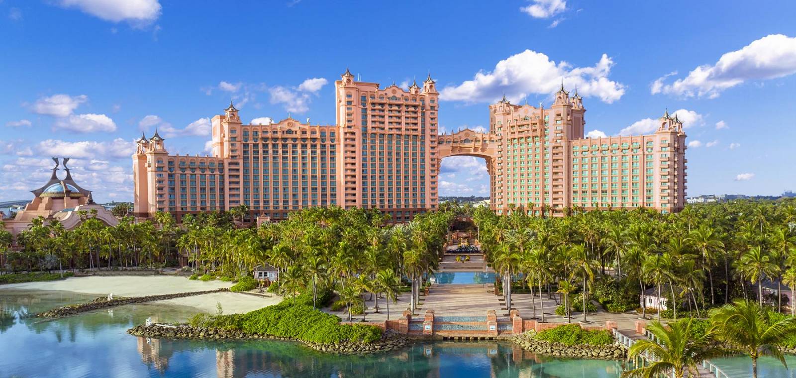 A exterior shot of The Cove, Atlantis Paradise Island. It is a pink resort in the Bahamas surrounded by palm trees and water.