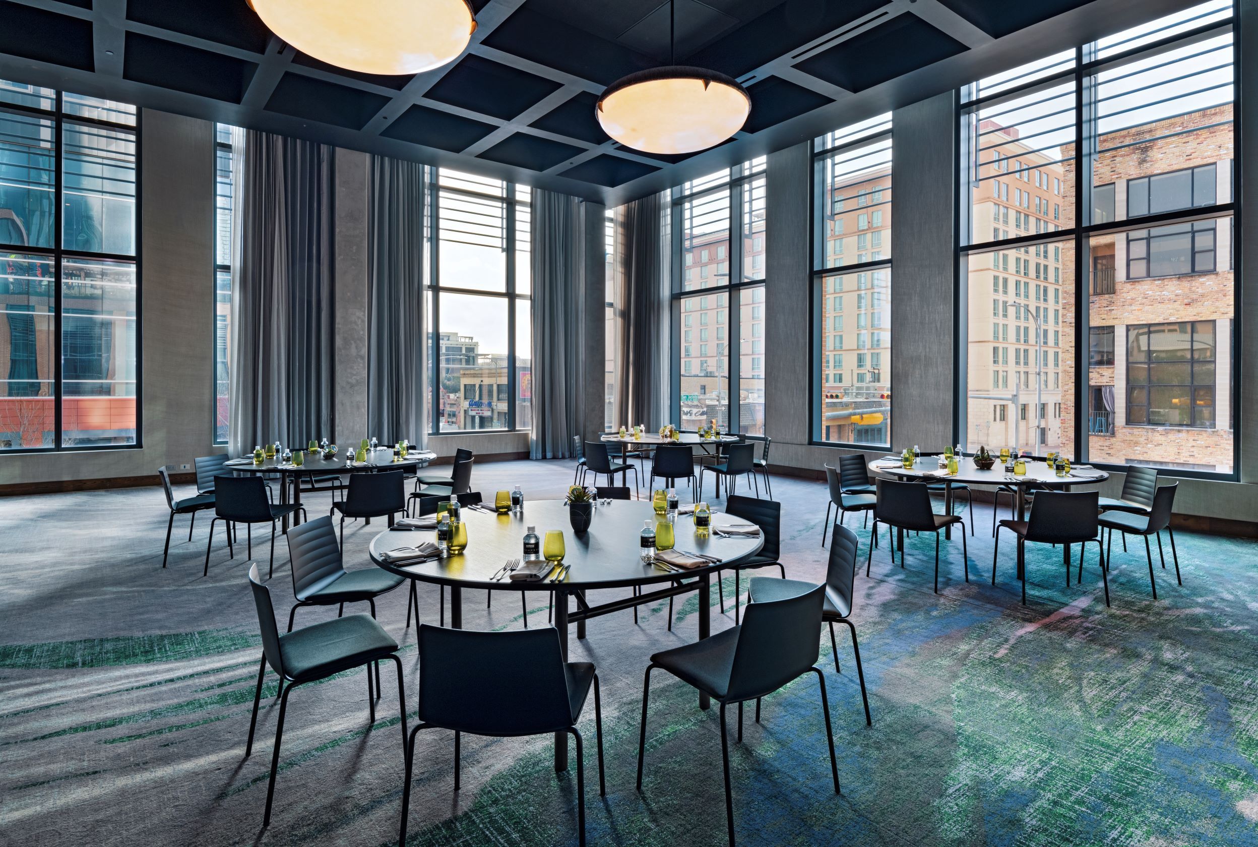 One of the meeting spaces in Thompson Austin. There are floor-to-ceiling windows and simple tables and chairs