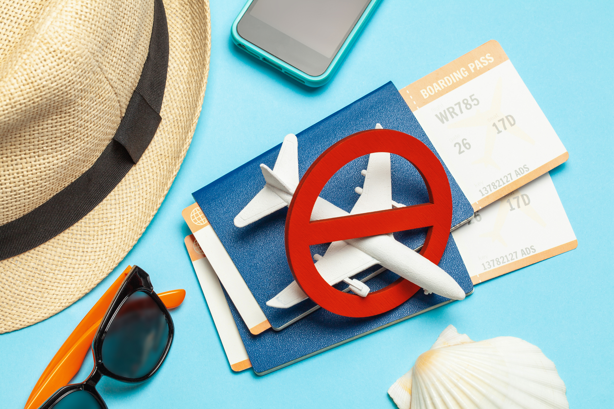 image of various items on blue background: a figurine airplane, brown fedora hat, sunglasses, two passports with boarding passes in them, and a smartphone