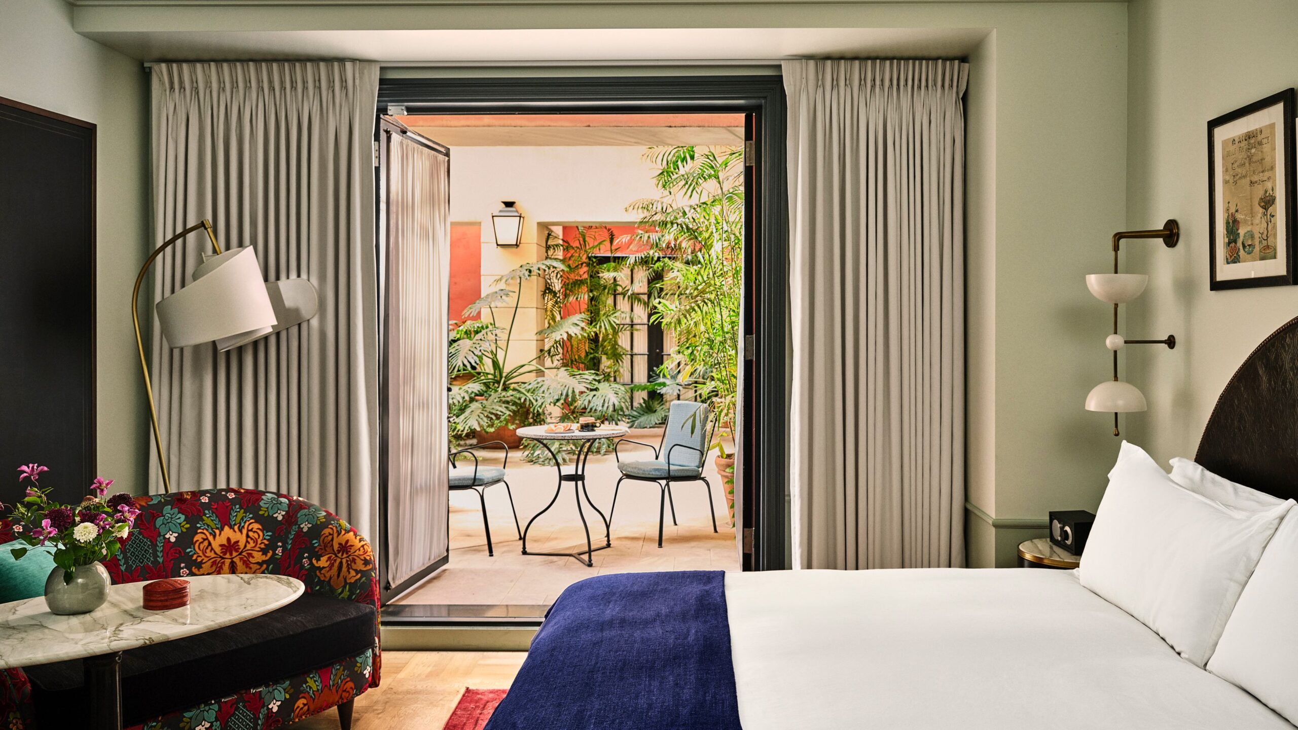 A patio room at Hotel Per La. A floral couch is to the left of a sliding door leading to a patio