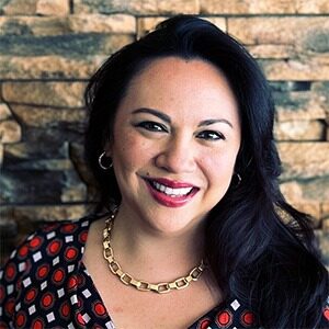 A portrait of Lauren Bruggemans. She is a brown woman with wavy black hair and a spotted blouse