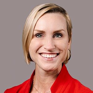 A portrait of Kate Thompson. She is a blonde white woman with hair in a bun and a red blouse