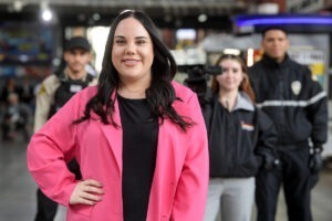 Woman in pink jacket with camera crew in background.