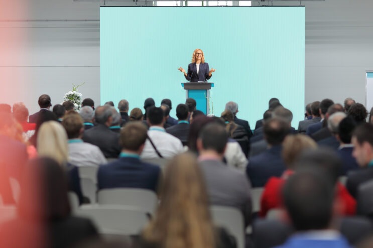 Woman giving a speech on a podium and people sitting in the audience at a conference