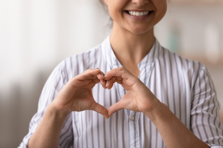 Close up cropped of smiling Indian woman showing heart shape gesture on chest