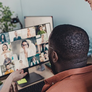 man wearing dark orange button up shirt talking to colleagues via video call