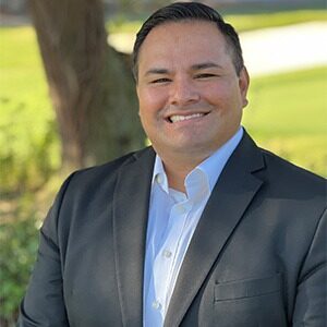 headshot of gilbert bolivar in gray sport coat and white dress shirt against background of grass