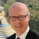 headshot of jay burress wearing black suit and red tie