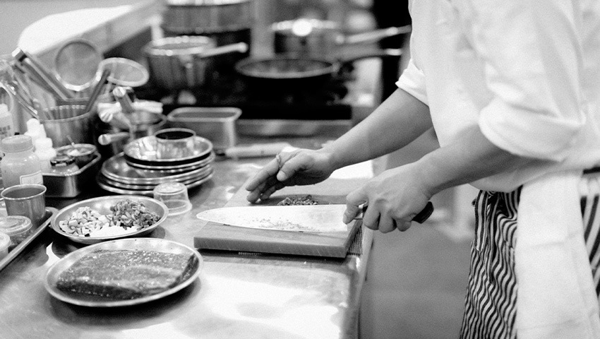 black and white photo of chef chopping herbs surrounded by various cooking tools and utensils 