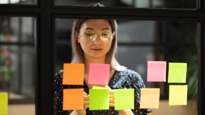 young businesswoman working and posting colorful sticky notes on glass wall