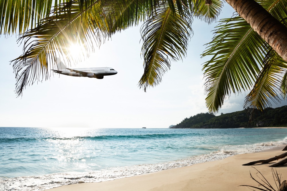 Airplane Flying In Cloudy Sky Over Island And Sea At Seychelles