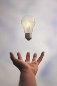 light bulb floating about hand with clouds in background