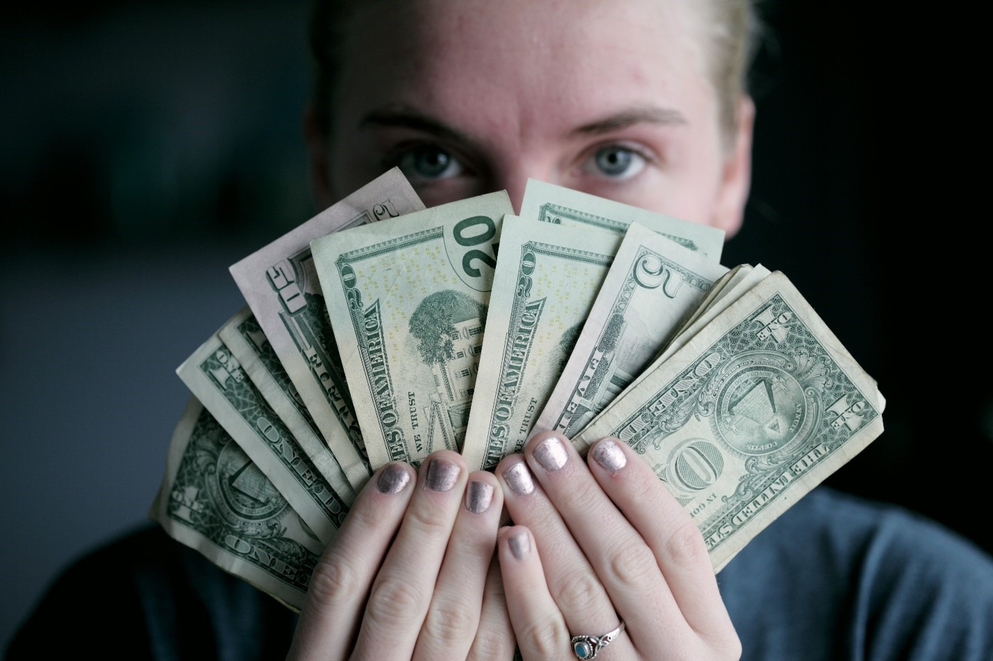 woman holding various US bills in front of face
