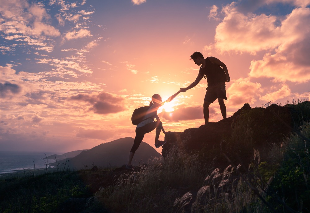 People helping each other hike up a mountain at sunrise