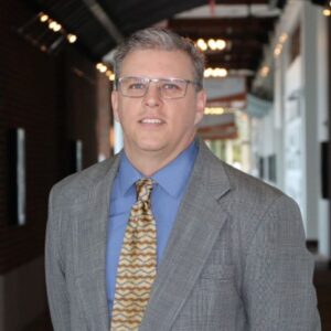 john sneed wearing blue dress shirt, gold tie and grey sport coat