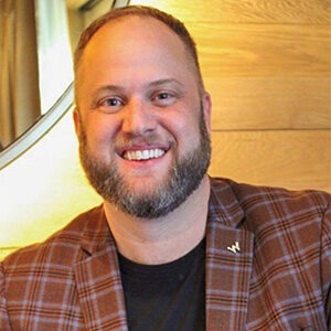 Derek Tueller wearing black shirt and red plaid sport coat