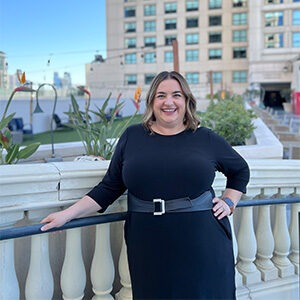 Megan Madrigal standing on bridge wearing black dress and black belt with gold buckle