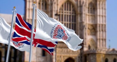 Flags with the emblem of the coronation of King Charles III and of UK waving with Westminster Abbey in the background