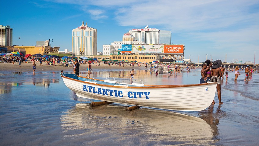 small white boat that reads "atlantic city" on beach, large number of people in backgroun