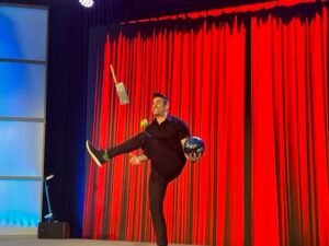 man on stage juggling ball and hatchet through legs