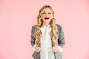 woman wearing pink sport coat and black dress shirt in front of pink backgroun