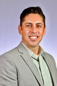 man smiling, wearing grey sport coat and green dress shirt