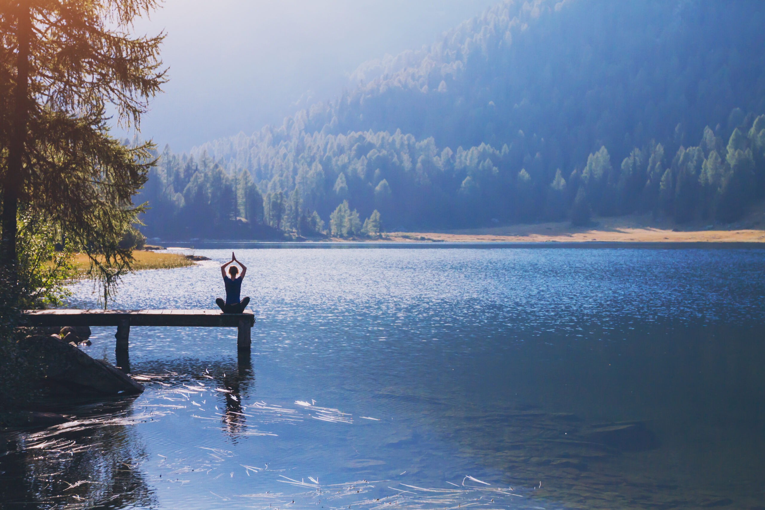 woman sitting on dock of lake with arms raised