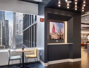 A table and two chairs under a window showing skyscrapers, next to a painting hung on the wall