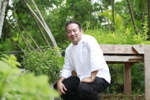 man in chef shirt sitting down among bushes