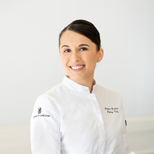 A woman in a chef's uniform smiles into the camera