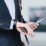 businessman with a cellphone and airplane ticket checking time on his watch