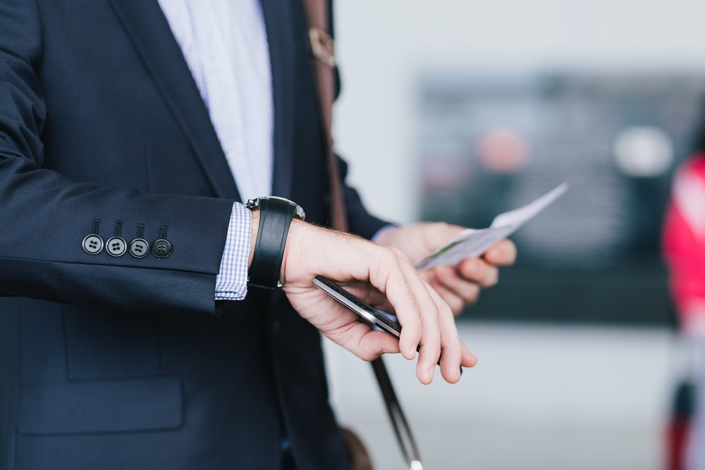 businessman with a cellphone and airplane ticket checking time on his watch