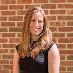 woman standing in front of brick wall, wearing sleeveless black top